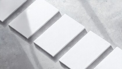 closeup of empty white rectangle poster mockups lying diagonally with soft shadow on neutral light grey concrete background flat lay top view open composition