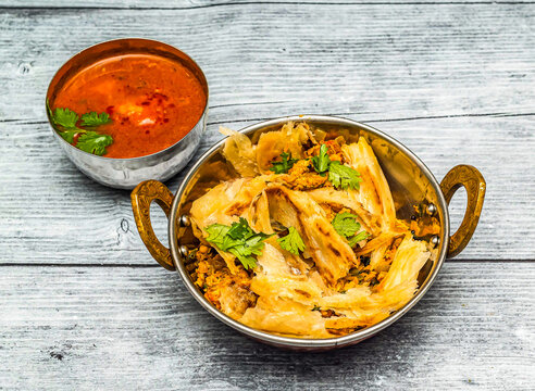 chicken kothu parotta with curry served in dish isolated on wooden table top view of indian spicy food