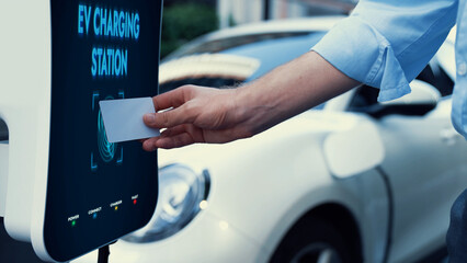Businessman pay electric vehicle's eco-friendly and sustainable energy scanning credit card at...