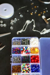 Box with colorful beads, string, wire, chain, scissors, pliers and hammer on dark background. Various jewelry making supplies. Selective focus.