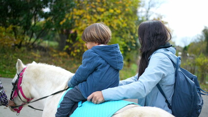 Child rides pony horseback, smiling mother and little boy son during fall season