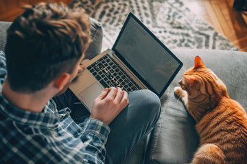 Handsome man working online from home by cat pet accompanied on his laptop - obrazy, fototapety, plakaty