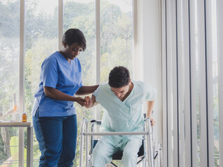 Portrait patient caucasian man with woman nurse carer physical therapist African-American two people talk helping support training sick person walk with crutches inside hospital indoor room service.