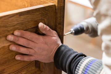 The man drills the wooden elements and holds them with his hand
