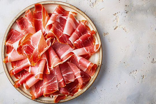 plato con jam&oacute;n serrano t&iacute;pico espa&ntilde;ol, cortado a mano en peque&ntilde;as lonchas, sobre superficie blanca 