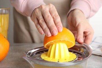 Woman squeezing orange juice at grey table, closeup - obrazy, fototapety, plakaty