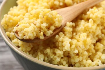 Tasty millet porridge and spoon in bowl on table, closeup