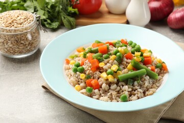 Tasty pearl barley porridge with vegetables on light textured table, closeup
