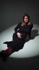 Pregnant young woman posing in a studio in a black dress