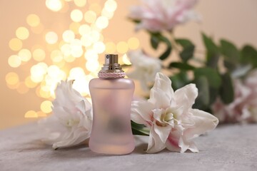 Bottle of perfume and beautiful lily flowers on table against beige background with blurred lights, closeup