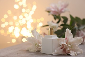 Bottle of perfume and beautiful lily flowers on table against beige background with blurred lights,...