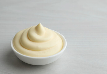 Tasty mayonnaise sauce in bowl on light wooden table, closeup. Space for text