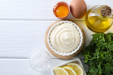 Fresh mayonnaise sauce in bowl and ingredients on white wooden table, flat lay. Space for text