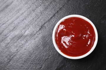 Organic ketchup in bowl on black table, top view with space for text. Tomato sauce