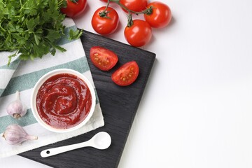 Organic ketchup in bowl, fresh tomatoes, parsley and garlic on white table, flat lay with space for text. Tomato sauce