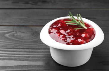 Fresh cranberry sauce in bowl and rosemary on black wooden table, closeup. Space for text