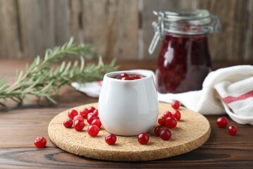 Cranberry sauce in pitcher and fresh berries on wooden table
