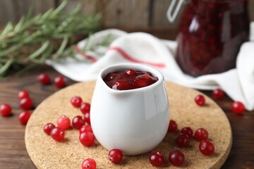 Cranberry sauce in pitcher and fresh berries on wooden table