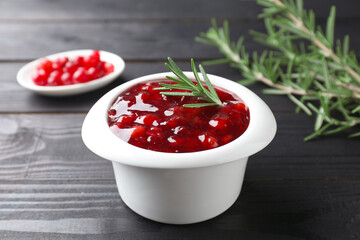 Fresh cranberry sauce in bowl and rosemary on black wooden table, closeup