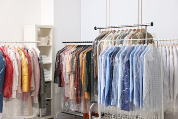 Dry-cleaning service. Many different clothes in plastic bags hanging from racks indoors