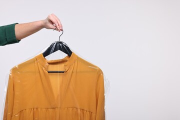 Dry-cleaning service. Woman holding dress in plastic bag on white background, closeup. Space for...