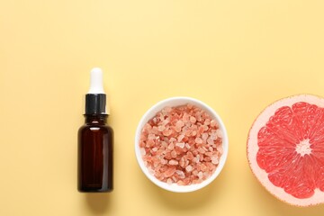 Flat lay composition with grapefruit essential oil on pale yellow background