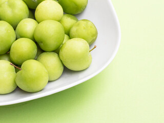 group of green plums in white bowl on green background. fresh  green plum