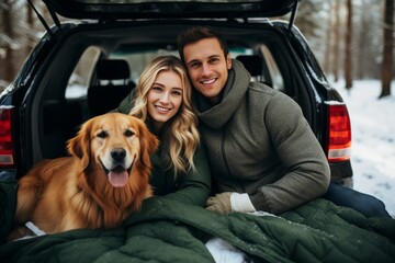 Young Caucasian tourist couple in winter outwear and their dog posing in front of their car in snowy forest. Cheerful travelers and their pet spend vacation together.