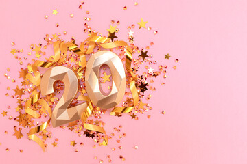 Golden number twenty, ribbons and stars confetti on a pink background. Festive concept with...