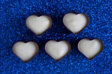 Five heart-shaped dark and white chocolate candies in dark and white chocolate. Festive blue shimmery background. Romantic concept. Photo. Bokeh. Selective focus