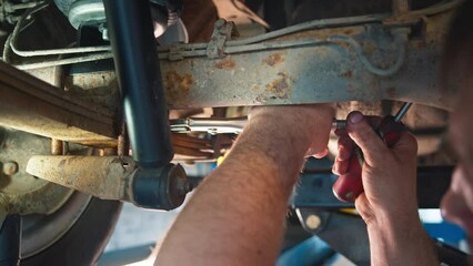 Mechanic's arm seen working on a vehicle's suspension, with tools in hand in a focused repair session at a car service center.