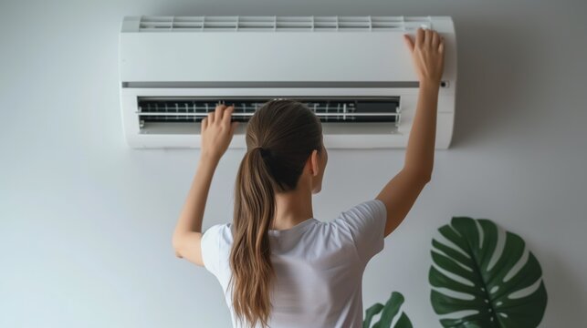 Young caucasian woman repair indoor air conditioner unit on wall, back view