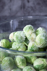 Frozen baby brussels sprouts defrosting in a glass bowl. On a dark stone background