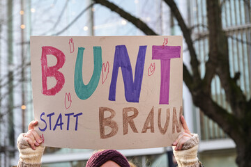 Woman holding a cardboard sign with the German text Bunt statt Braun (Colorful instead of Brown), as protest against racism and neo-Nazi fascism on a demonstration in Lubeck Germany, January 22, 2024 - obrazy, fototapety, plakaty