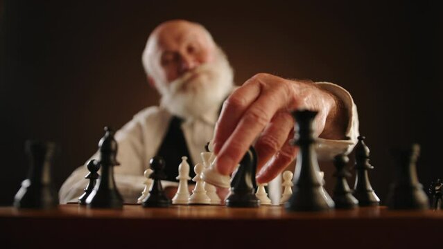 An elderly man strokes his beard in thought, then strategically moves his knight, capturing the opponent's knight, and gestures invitingly for the next move. Camera 8K RAW. 