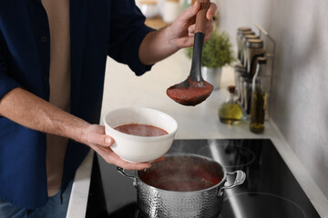 Man pouring delicious tomato soup into bowl in kitchen, closeup