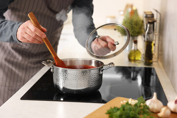 Man cooking tomato soup on cooktop in kitchen, closeup