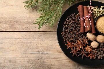 Dishware with different spices and fir branches on wooden table, flat lay. Space for text