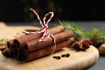 Cinnamon sticks and other spices on table against black background with blurred lights, closeup