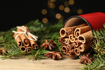 Many cinnamon sticks, anise stars and fir branches on wooden table, closeup. Space for text