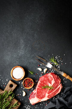 Raw meat steak. Beef steak with spices on black background. Top view with copy space.
