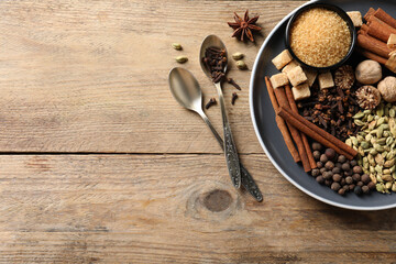 Plate with different aromatic spices and spoons on wooden table, flat lay. Space for text