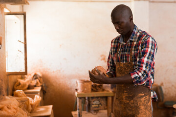 Concentrated African craftsman working at pottery workshop, moulding wet clay in hands