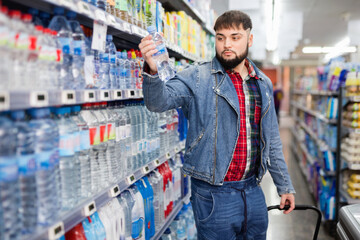 Portrait of focused young cheerful positive smiling man purchasing bottled water in grocery store