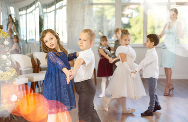 Joyful minor schoolboys and schoolgirls training valse dance in events salon adorned with Xmas tree