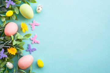 Fototapeta na wymiar Easter background or greeting card on blue. Eggs, spring leaves, flowers and colored butterflies. Flat lay with copy space.