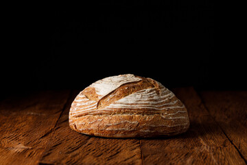 Fresh wheat rustic sourdough loaf bread on a wooden table black background. Close up shot	
