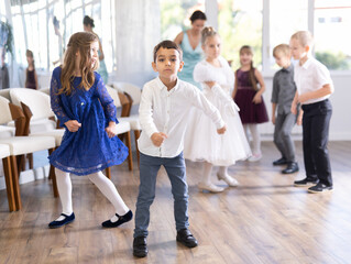 Joyful schoolboys and schoolgirls of primary classes training twist dance in events salon