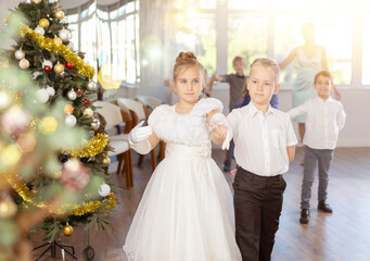 Pleased minor schoolboys and schoolgirls standing in row performing dance position in events salon...