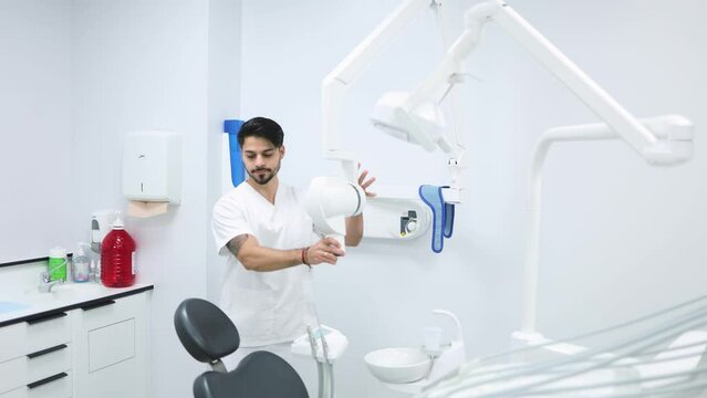 Male dentist setting up the UV machine for teeth whitening in a modern dental clinic. Young dentist preparing the ultra violet machine to do a teeth whitening for a patient in the dental clinic.